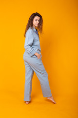 Smiling young girl in pajamas home wear posing while resting at home isolated on yellow background studio portrait. Relax good mood lifestyle concept.