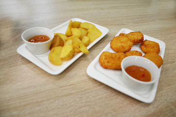 chicken nuggets and fried potatoes on a white plate on a table in a cafe or restaurant