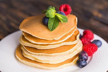 Pancakes with blueberries and raspberry on wooden background. Breakfast and traditional meal.