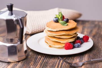 Pile of pancakes with blueberries and raspberries for breakfast on wooden table.