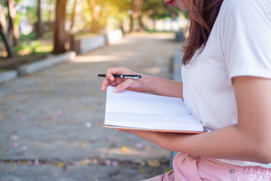 a young woman's hand by writing a pen on a park notebook in the evening.