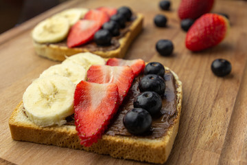Delicious toast bread with chocolate topping, banana, strawberry and blueberry on a wooden board. Concept of tasty and health breakfast. 