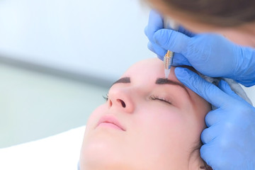 Cosmetologist making eyebrows microblading procedure in beauty salon for girl using tattoo apparatus, face closeup. Beautician in gloves is doing permanent makeup to woman. Beauty industry concept.