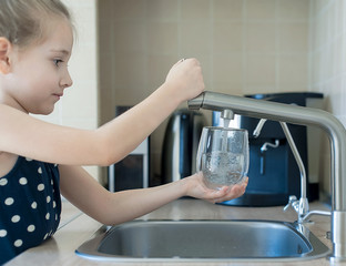 Child is holding a transparent glass. Filling cup beverage. Pouring fresh drink. Consumption of tap water contributes to the saving of water in plastic bottles and to the protection of the environment