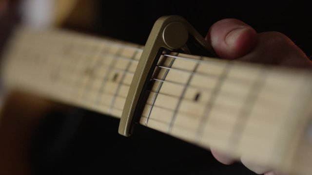 Guitar player places capo on and removes capo from 5th fret on electric guitar during practice session, slow motion.