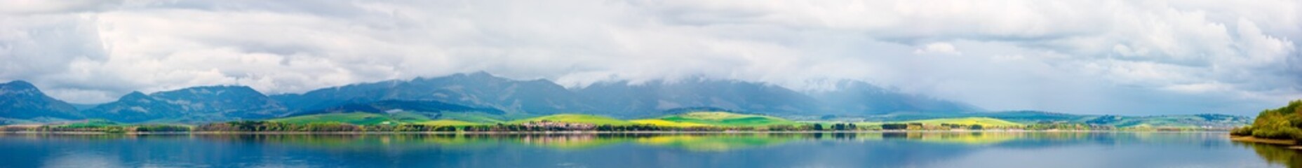 Fototapeta na wymiar panorama of lake in mountains. cloudy day in springtime. beautiful scenery of high tatra mountains in dappled light. gorgeous landscape of liptovska mara, slovakia