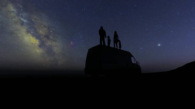 Silhouettes of people stand on the roof of the car and look at the stars. Family mother daughter son father. Happy family. 4k
