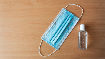 Gel antiseptic and blue medical mask lie on a wooden background. Coronavirus epidemic concept with...