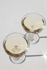 Two glasses of sparkling wine on the pink table in natural sunlight with shadows.
