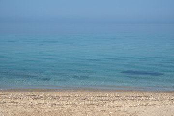 Fototapeta na wymiar The calm surface of the sea and a deserted sandy beach. Small waves and blue sky. Halkidiki, Greece.