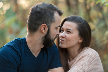 Portrait of young beautiful couple in the Park. They look at each other. In the background of leaves of trees.