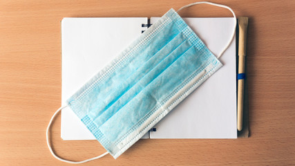 Notebook with eco pen and blue medical mask lie on a wooden background. Coronavirus epidemic...