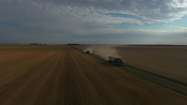 Drone shot of two semi trucks driving on dirt roads surrounded by fields