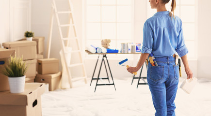 Pretty smilling woman painting interior wall of home with paint roller