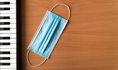 Piano keys and blue medical mask lie on a wooden background. Coronavirus epidemic music concept with copy space.