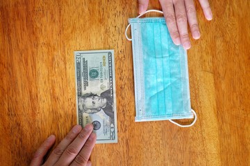 Hands exchanging 20 dollar bill for a surgical face mask signifying a spike in price of face mask...