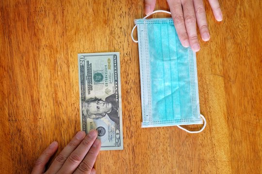 Hands Exchanging 20 Dollar Bill For A Surgical Face Mask Signifying A Spike In Price Of Face Mask During The Corona Virus Pandemic Of 2020.