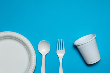 disposable spoon, fork, glass and plate of corn starch on a blue background. biodegradable...