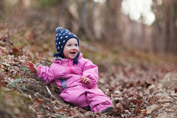 A small child walks in the autumn forest, a girl dressed in a pink jumpsuit and a hat, fresh forest air is good for children's health, The kid sits on dry fallen foliage