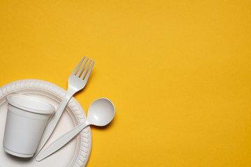 disposable plate, glass, spoon and fork of corn starch on a yellow background. biodegradable eco...
