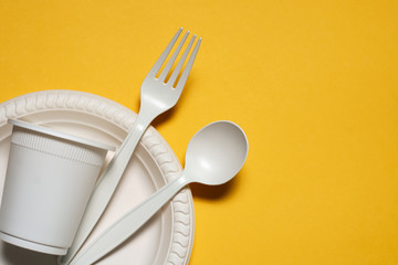 disposable plate, glass, spoon and fork of corn starch on a yellow background. biodegradable eco...
