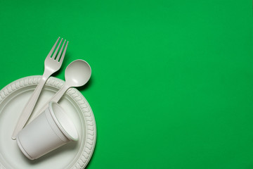disposable spoon, fork, glass and plate of corn starch on a green background. biodegradable...