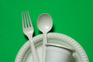 disposable spoon, fork, glass and plate of corn starch on a green background. biodegradable...