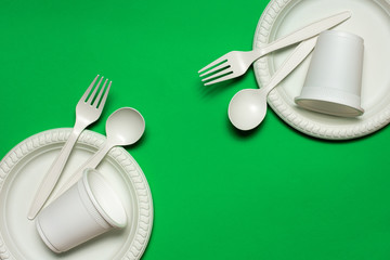 two sets of disposable spoons, forks, plates and glasses of corn starch on a green background....