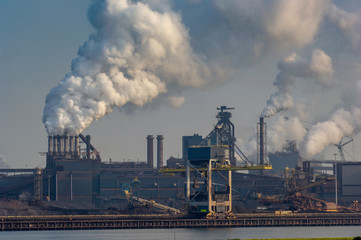 Heavy industry in the port of Ijmuiden Netherlands billowing pollution into a blue sky.