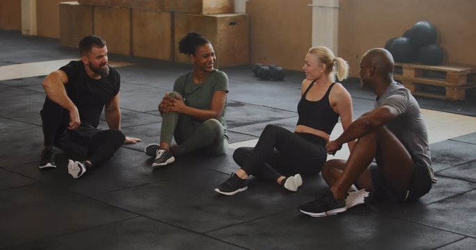 Diverse group of young friends in sportswear
laughing and talking together on a gym floor after a workout
