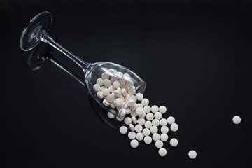 The glass with the white pills spilling out of it lies diagonally on a mirrored black background. Concept-healthy food and nutritional supplements as a way to enjoy life.