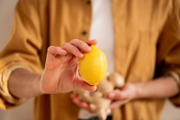 Woman in a beige jacket holding a lemon between two fingers