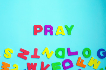 Word PRAY made of colorful letters on blue background.