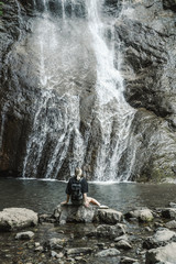 one a girl with a backpack sits on stones with her back and looks at a mountain waterfall, 
Georgia waterfall, small mountain waterfall,