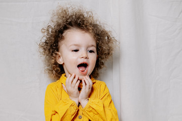Portrait of a girl with bright sincere baby emotions. Little curly girl posing for a photo
