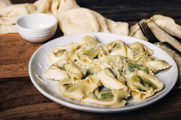 Italian ravioli with spinach, ricotta and parmesan cheese on top, close-up on a plate. rustic style on wooden table.