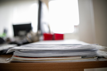 Pile of documents on desk stack up high waiting to be managed.