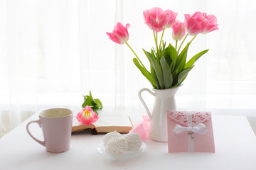 postcard good morning. Still life : a Cup of tea, a bouquet of pink tulips, marshmallows on a light background near the window.