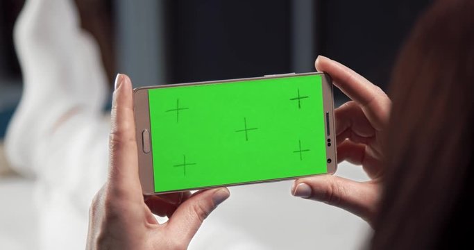 Close up of smartphone with green empty screen that holding woman in hands while sitting on couch. Young lady using digital device during free time at home.