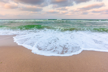 golden cloudy sunset above the green sea waters. waves crashing the sandy beach. clear horizon. changing windy weather
