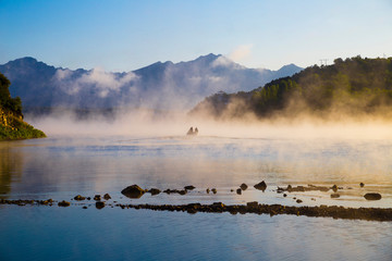 Concept mysterious landscape of a boat with two fisherman at misty lake