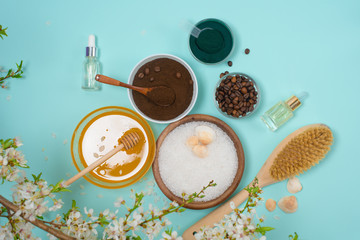 Spa products for home body care for cellulite and acne. sea salt, coffee scrub, honey in plates on a blue background and a flower branch. spring composition of organic ingredients