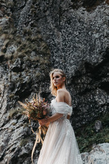 Fototapeta na wymiar noise effect, selective focus: attractive girl dressed in chic long wedding dress on a background of mountain rocks, model posing for promotional photos for wedding salon