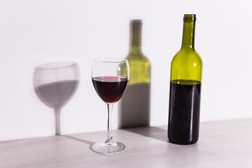 A glass of wine and a bottle casts a long shadow from the evening sun.