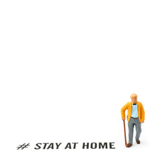 Old man and coronavirus outbreak. Small figurine and text STAY AT HOME on white background.