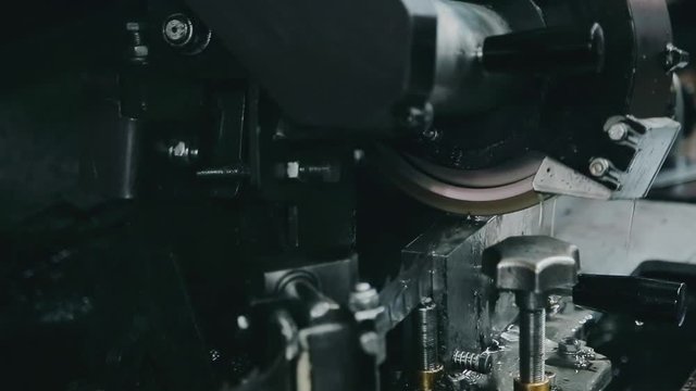 Sharpening of a band saw on an automated grinder, close-up shooting. The grinding disc touches the saw and is dampened with oil, sparks fly.