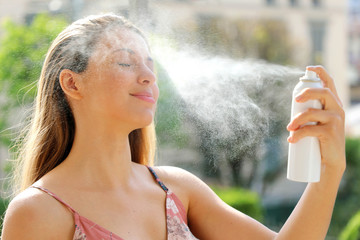 Young woman spraying Thermal Water on her face outside. Thermal water used for skin care, fix...