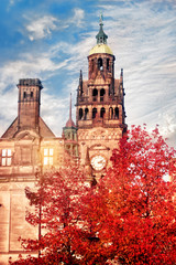 Obraz premium Yellow town hall with clock and green dome and red tree in front of it at the sunset against cloudy blue sky in the Autumn
