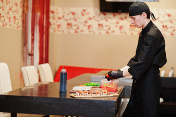 Professional chef wear in black making sushi and rolls in a restaurant kitchen of japanese traditional food.