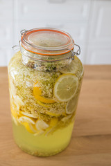 Preparing homemade elderflower syrup. Elder flowers with lemon slices in a glass jar to make a refreshing drink. Top view, vertical shot.